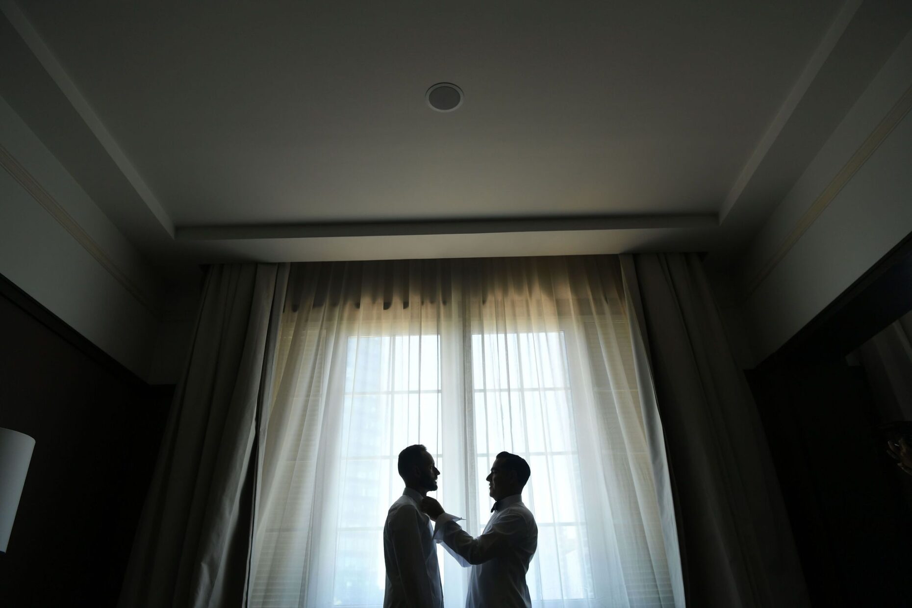 Two grooms in front of giant window in daylight