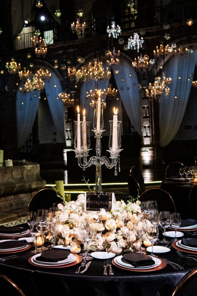 Wedding reception table with a chandelier from above, candles, custom menus, and flowers.