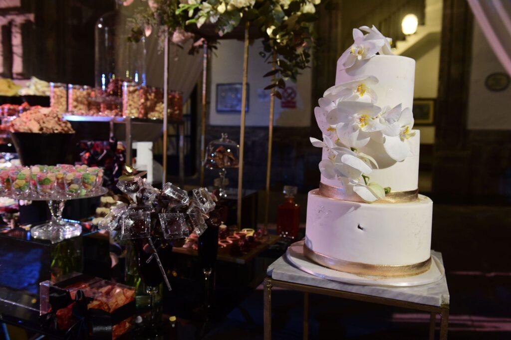 white three tier cake adorned with orchids next to candy trays