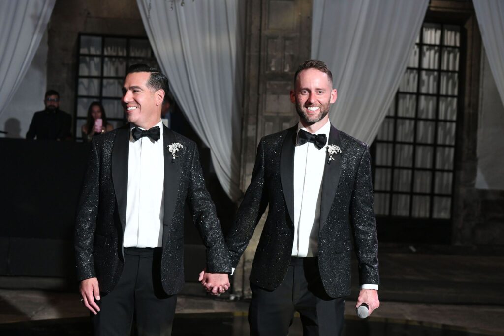 Two groom holding hands wearing glitter tuxedos