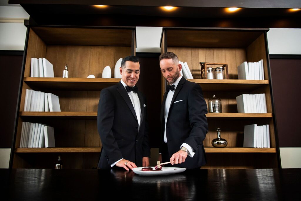 two grooms break a tiny red heart on a plate