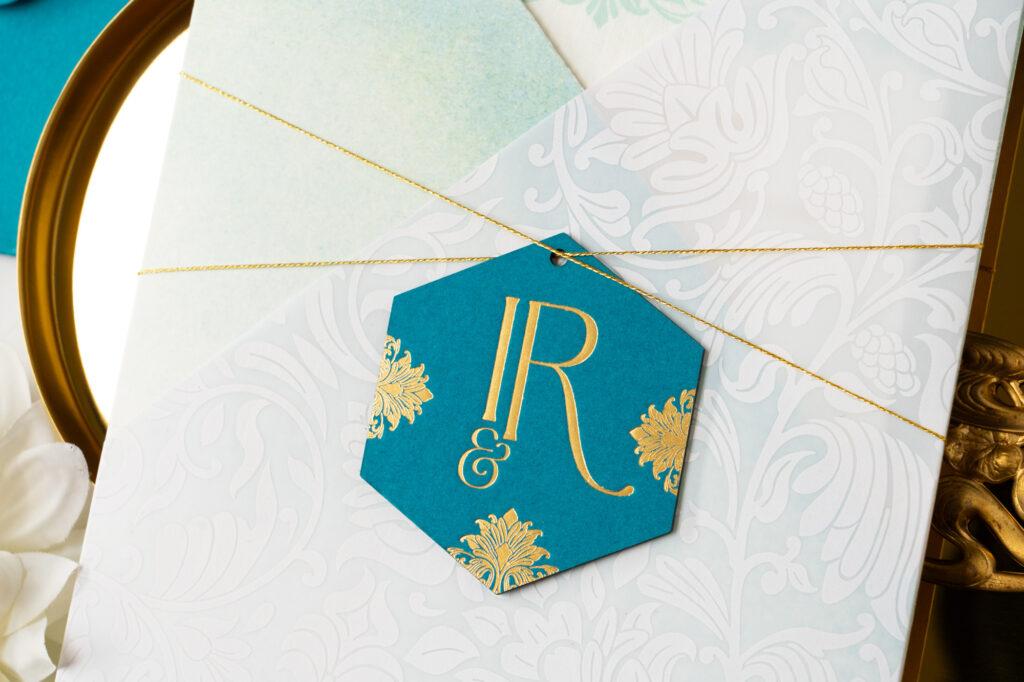 Teal and gold foil medallion with custom designed monogram for a multi-cultural wedding invitation